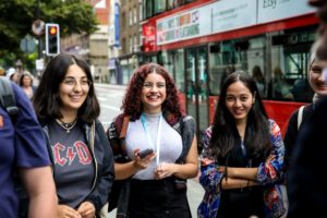 Three students standing in a London street with bus going by