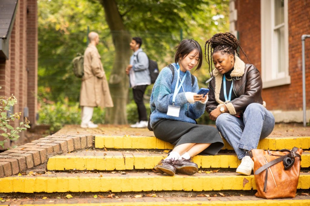 Two students sitting on stairs outdoors in Manchester